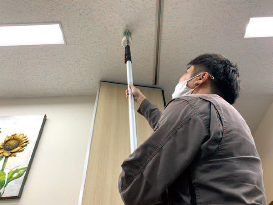 作業員が天井の火災報知器を専用器具で点検している様子